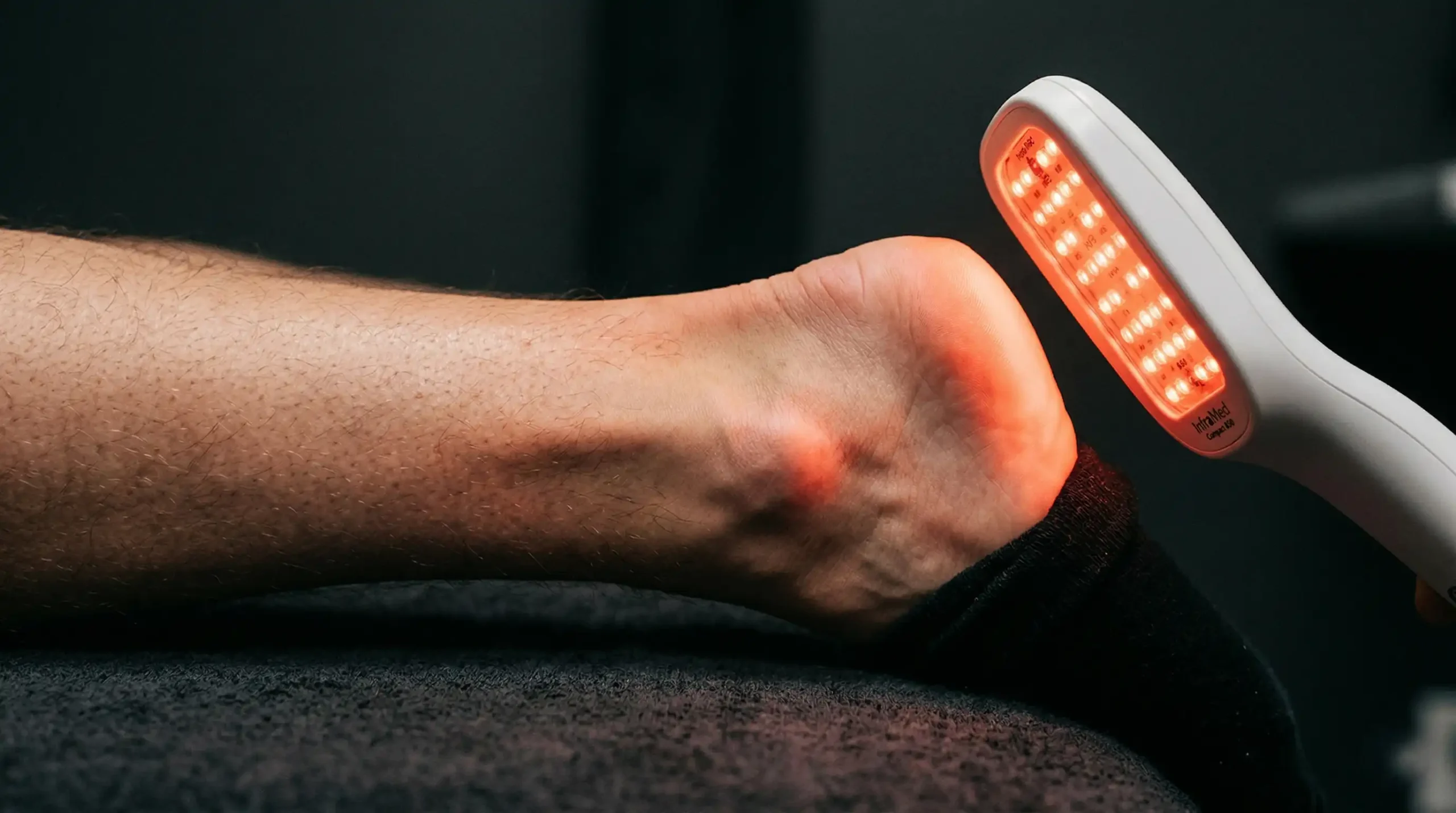 Person applying near-infrared 850nm red light therapy device to Achilles tendon for photobiomodulation tendinopathy treatment protocol